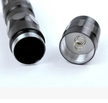 Small black aluminium LED flashlight with a strong beam, shown next to a AA battery for scale.