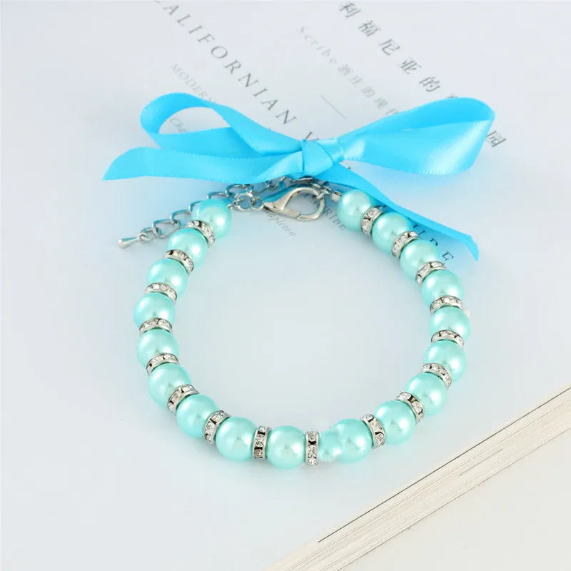 Small dog wearing an adjustable blue pearl and rhinestone necklace with a ribbon bow.