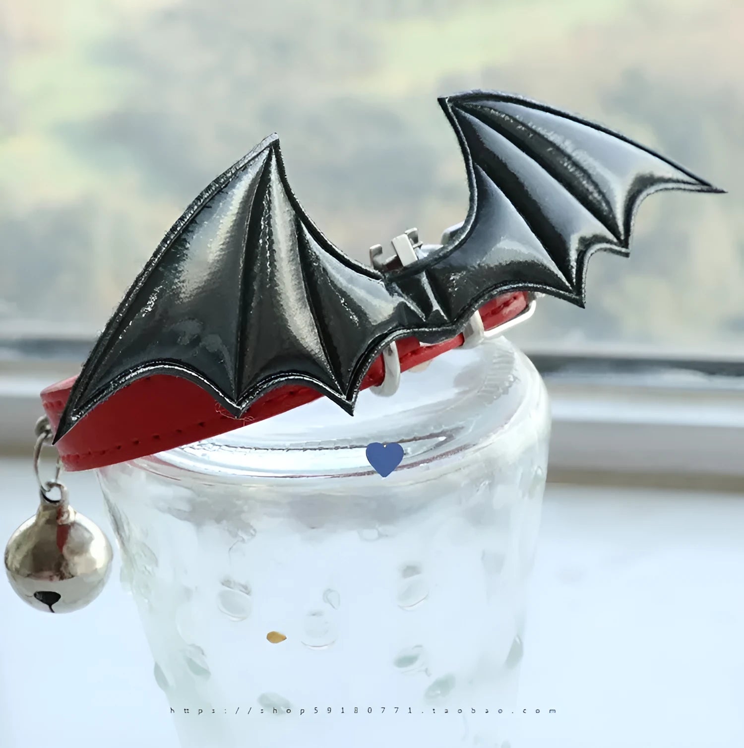Small black patent leather dog collar with decorative devil wings design on a white background.