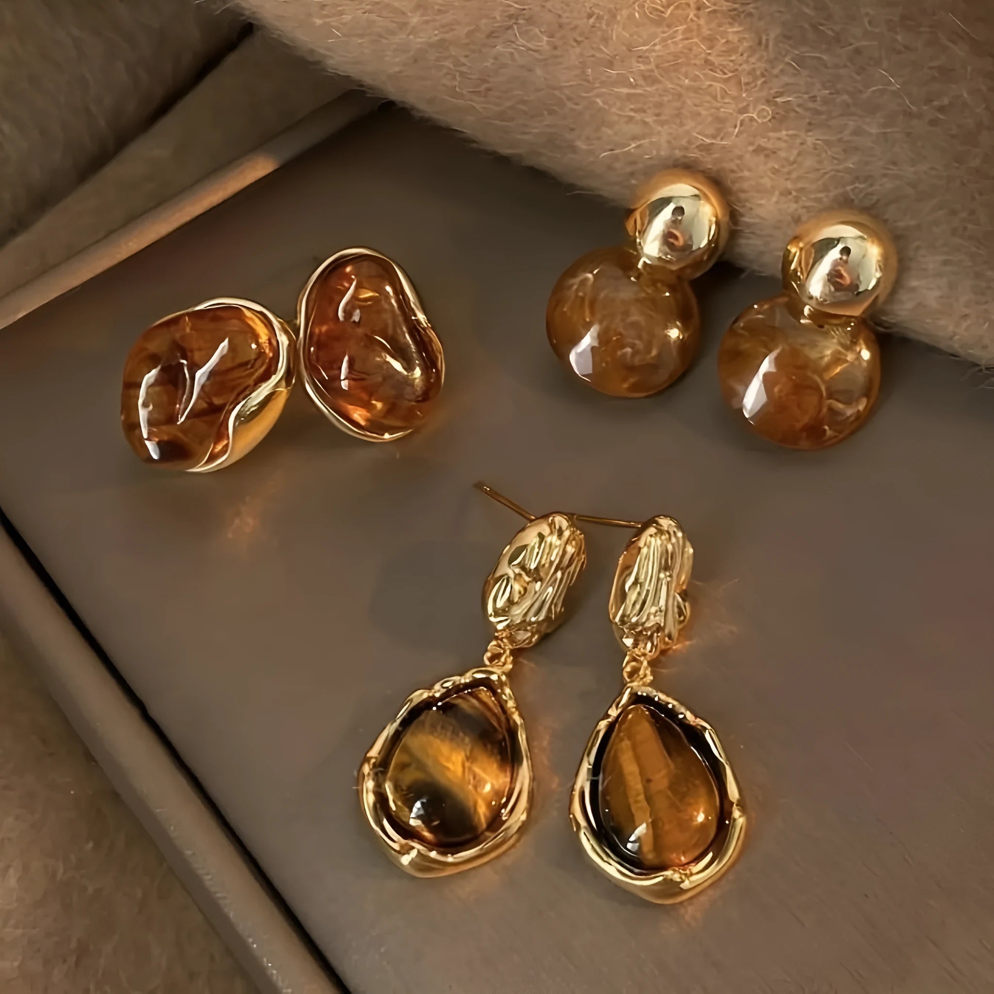 Handmade geometric earring set showing three styles: round piece, irregular amber, and water drop tigereye studs with tassels.