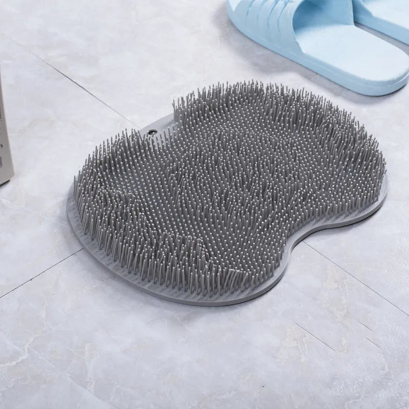 Orange suction cup bath brush with silicone bristles for foot and back cleaning on a bathroom floor.