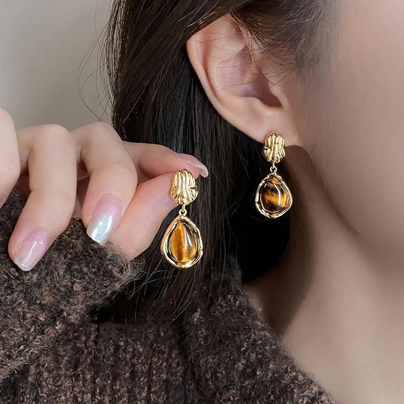 Handmade geometric earring set showing three styles: round piece, irregular amber, and water drop tigereye studs with tassels.