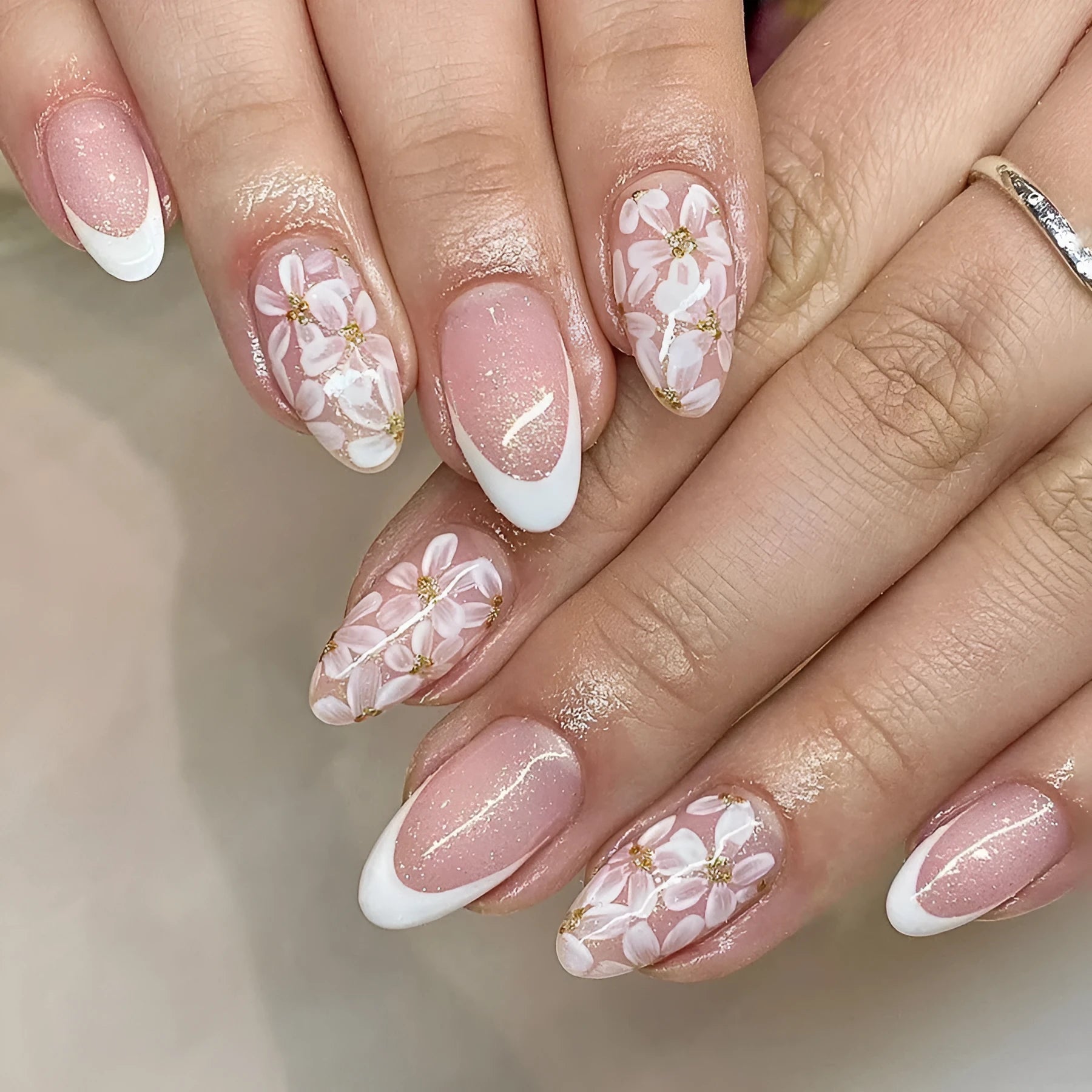 Short almond shaped false nails with French style gloss and glittering powder flower accents