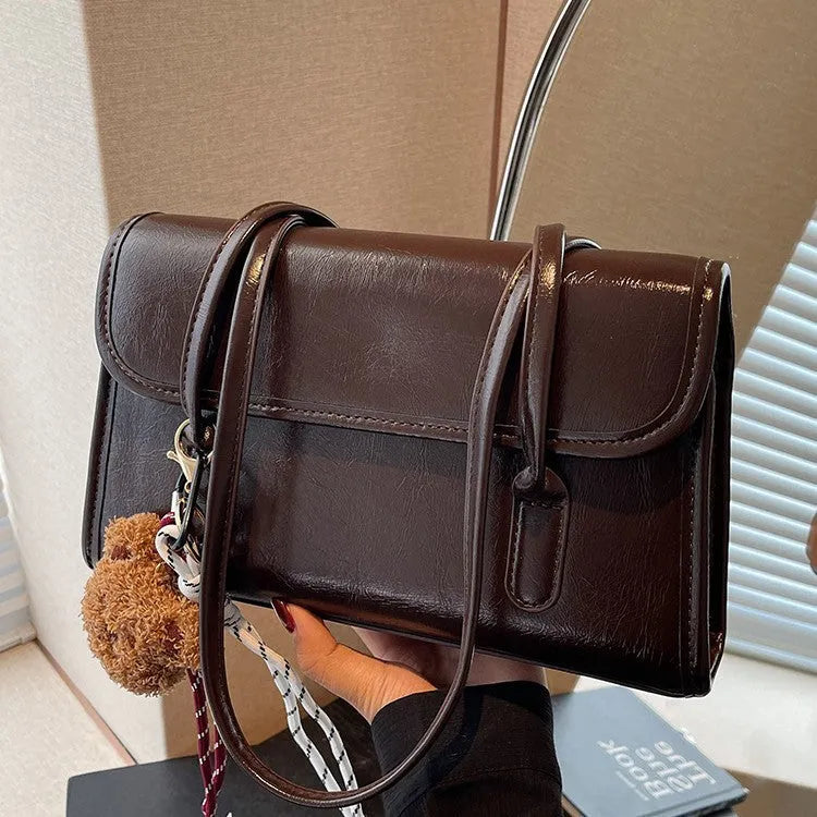 Brown women's square PU shoulder bag with a detachable pendant on a table