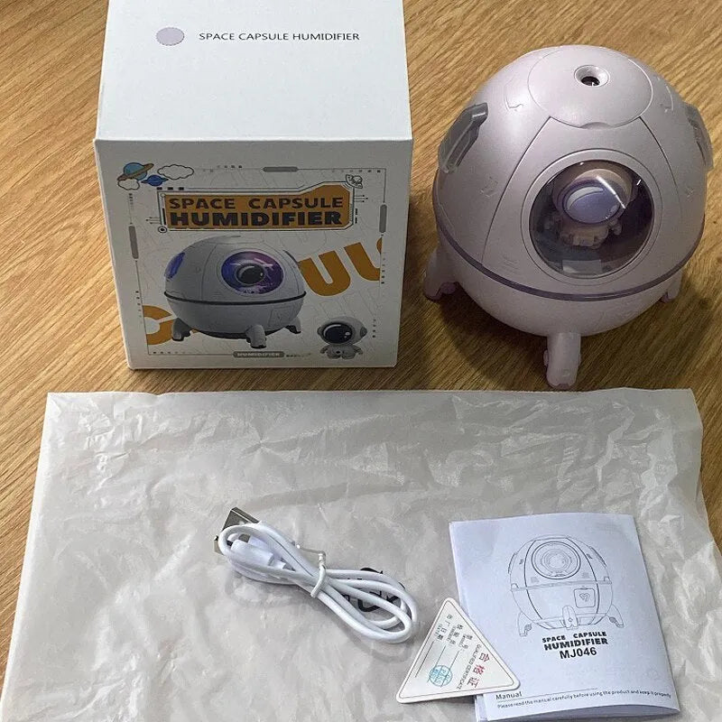 Purple astronaut-shaped USB desktop humidifier with LED light on a desk next to a laptop.