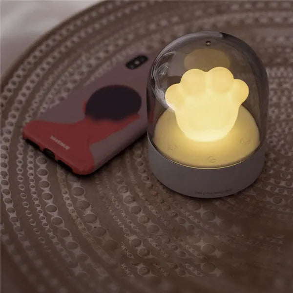 Pink and grey cat paw shaped USB night light with a music box feature on a desktop.