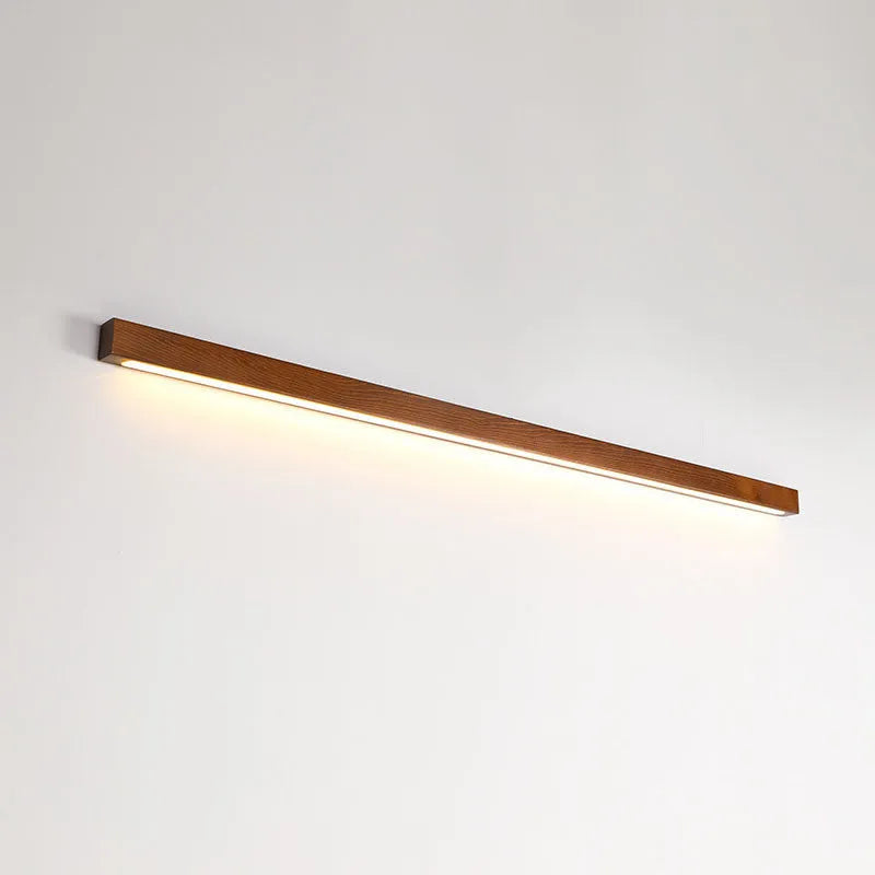 Walnut colour minimalist wooden and acrylic strip wall lamp in three length options on a white wall.