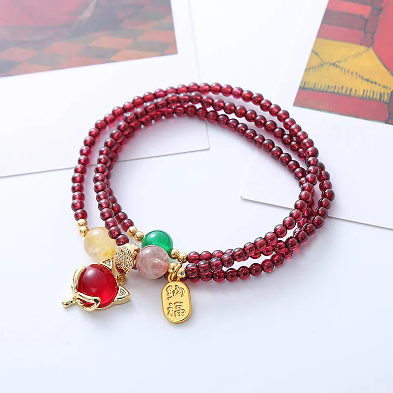 Purplish red garnet fox charm bracelet with adjustable rope on a wrist.