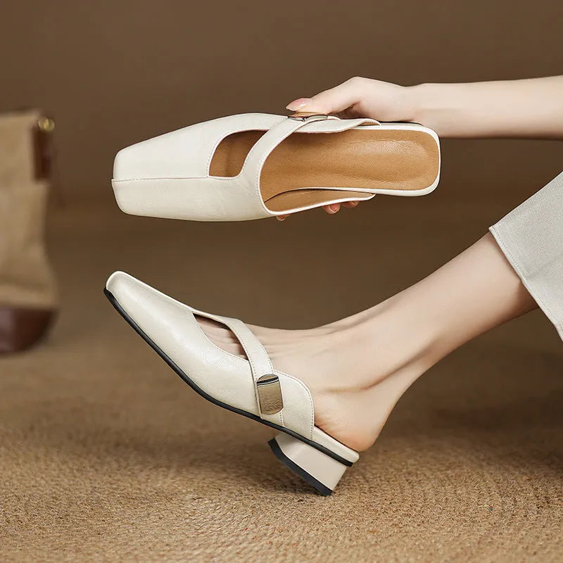A pair of beige square head low heel slippers with a rubber sole on a wooden deck.