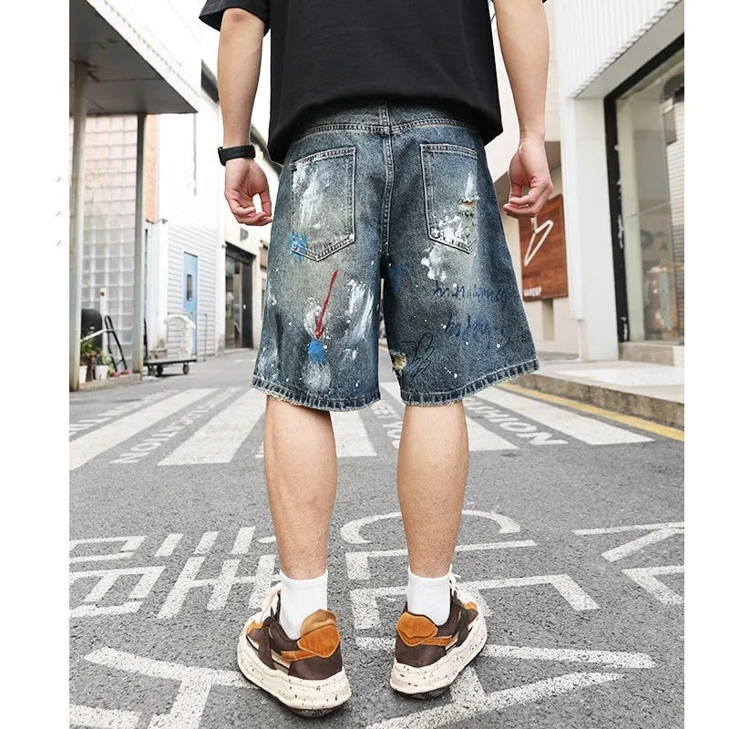 Blue men's ripped denim shorts with a graffiti pattern and zipper fly, laid flat.