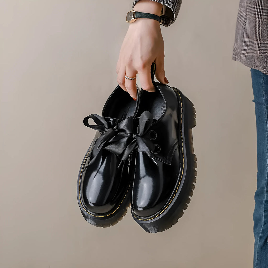 Black thick-soled women's lace-up shoes with ribbon and cross strap detailing on a white background