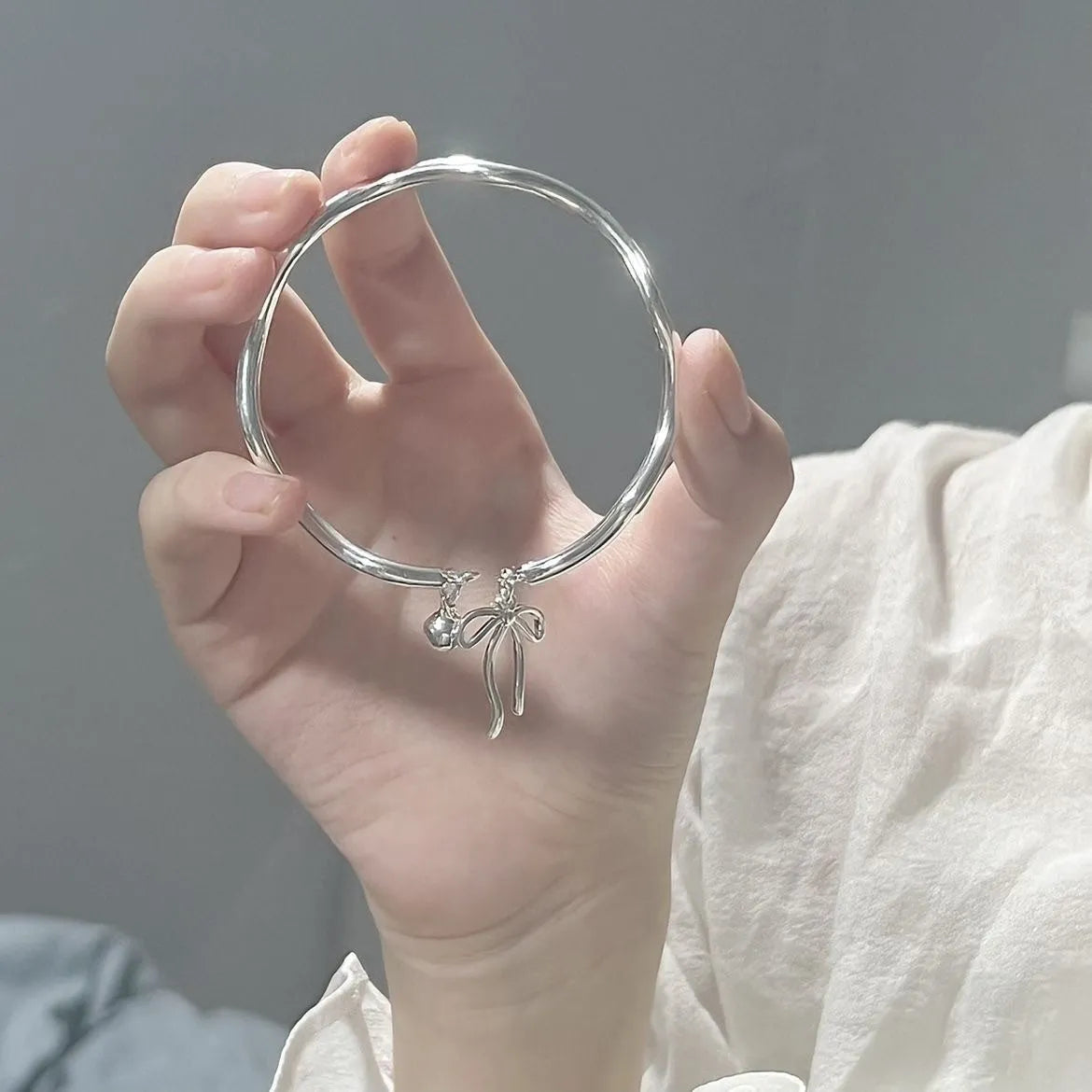 Silver adjustable bracelet with a fixed bow charm on a wrist.