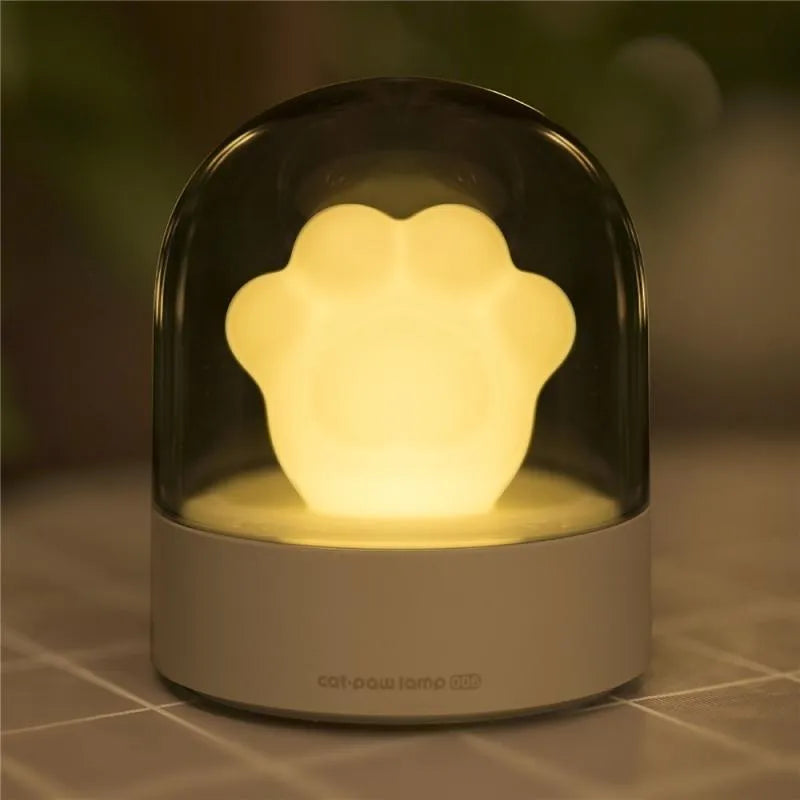 Pink and grey cat paw shaped USB night light with a music box feature on a desktop.
