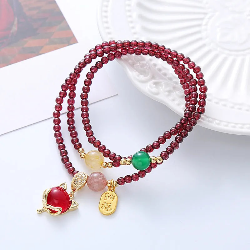 Purplish red garnet fox charm bracelet with adjustable rope on a wrist.