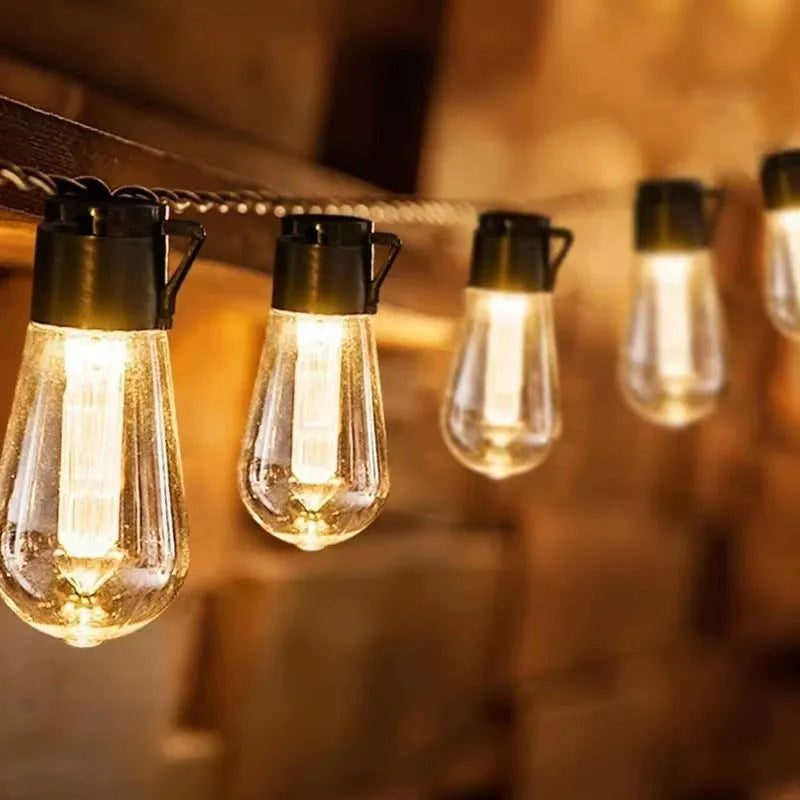 Retro glass infusion bottle-shaped outdoor string lights draped in a garden setting.