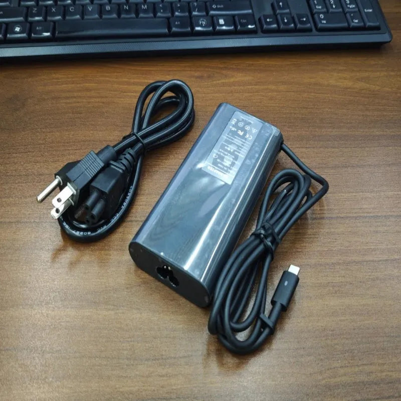 Black oval 65W USB-C laptop power adapter with Type-C port and multiple international power cords