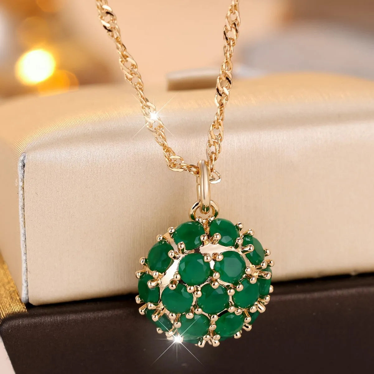 Champagne gold geometric pendant necklace with a round emerald stone and diamond accents on an adjustable chain.