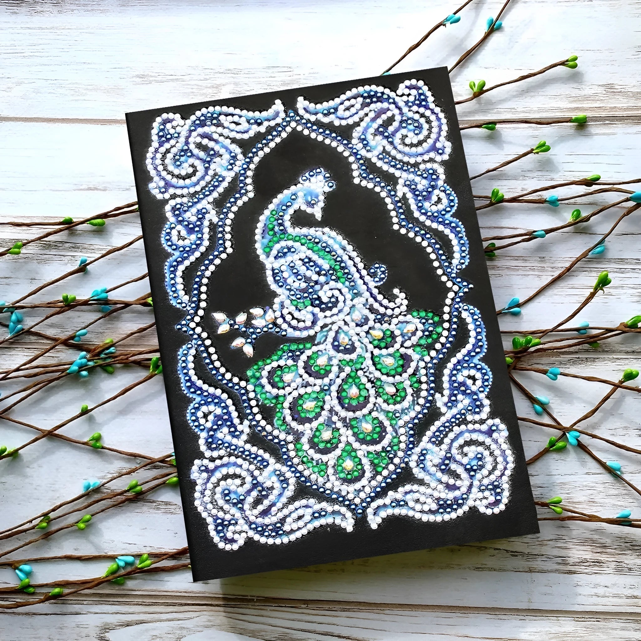 Black hardcover A5 diamond painting notebook with peacock beauty design, showing dimensions 142mm by 207mm.