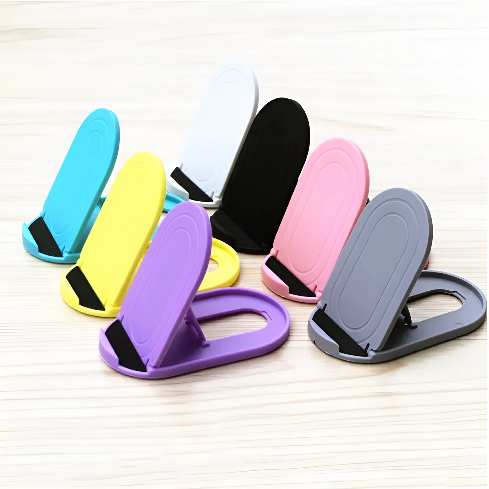 Plastic mobile phone stand with adjustable bracket in six colour options on a wooden desk