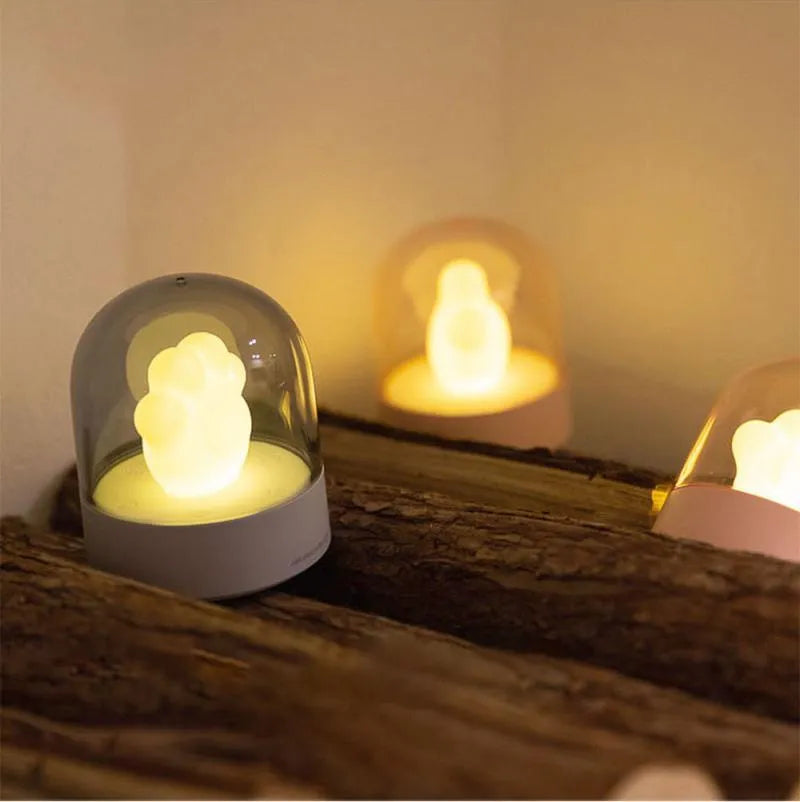 Pink and grey cat paw shaped USB night light with a music box feature on a desktop.