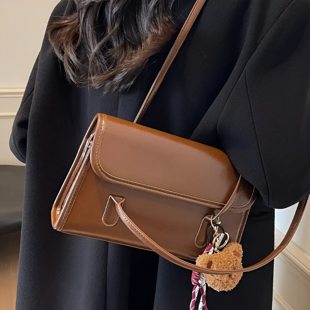 Brown women's square PU shoulder bag with a detachable pendant on a table