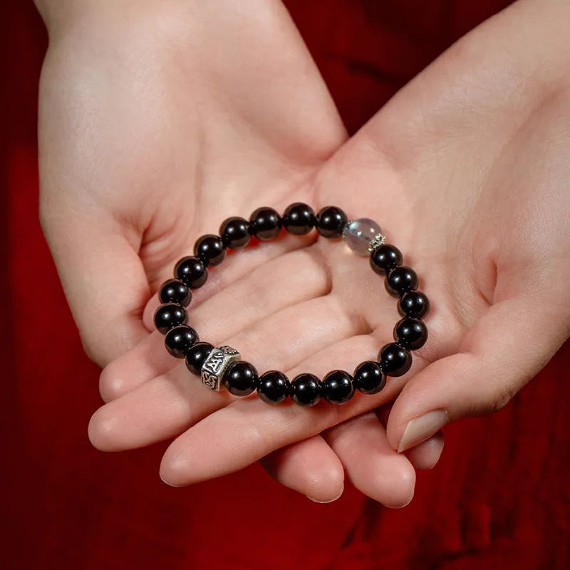 Dark 8mm obsidian bracelet with carved Chinese zodiac animal design on a wrist.