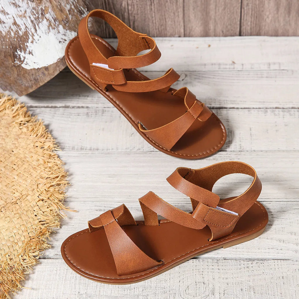 Women's flat sandals with Velcro strap on a round toe, shown in black, brown, and multi-colour options.