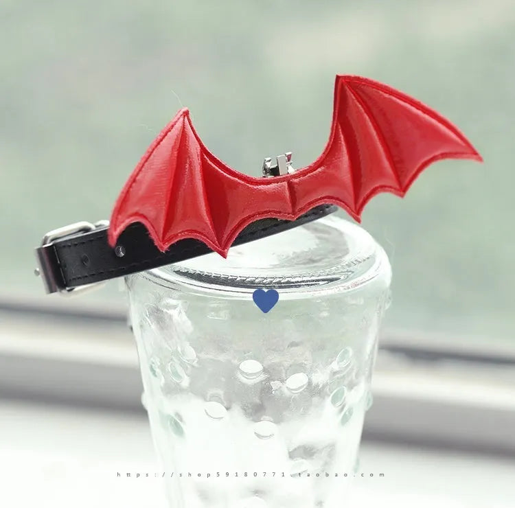 Small black patent leather dog collar with decorative devil wings design on a white background.