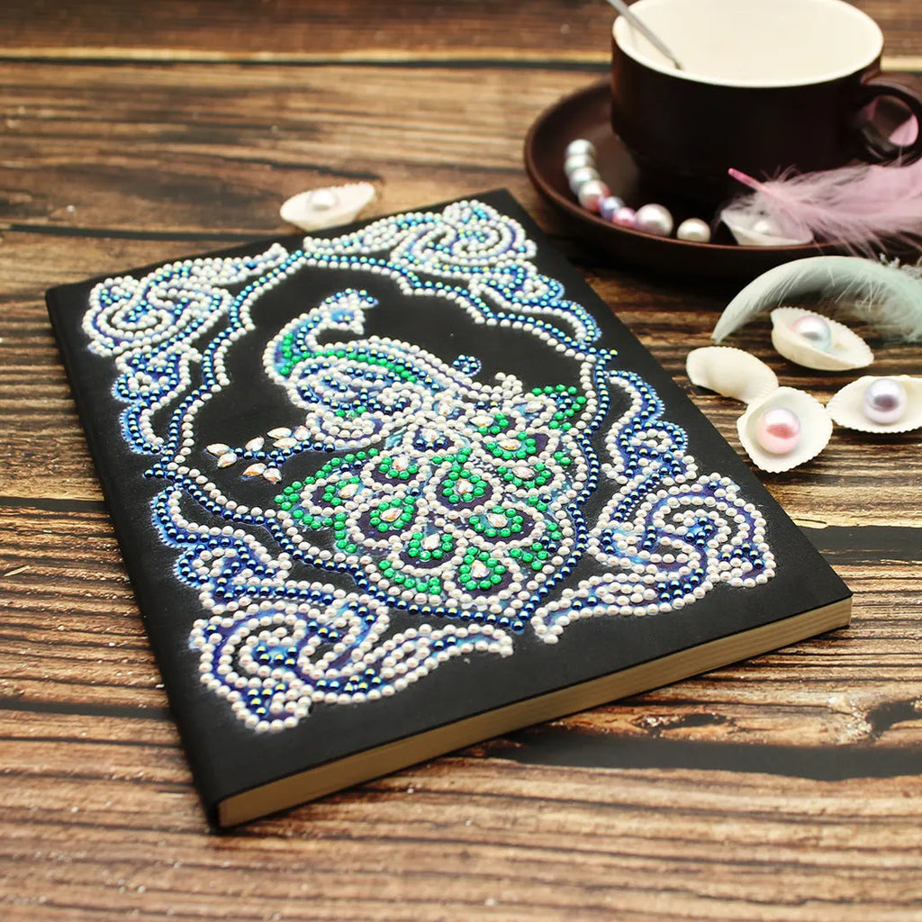 Black hardcover A5 diamond painting notebook with peacock beauty design, showing dimensions 142mm by 207mm.