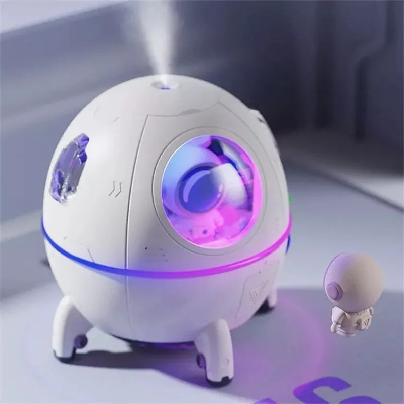 Purple astronaut-shaped USB desktop humidifier with LED light on a desk next to a laptop.