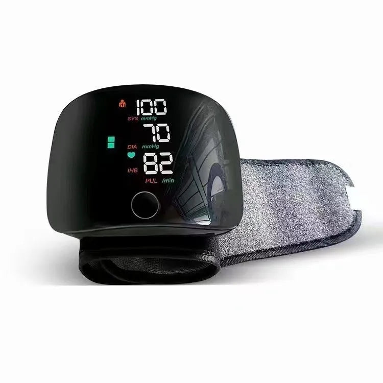Black wrist blood pressure monitor with USB charging port on a table.
