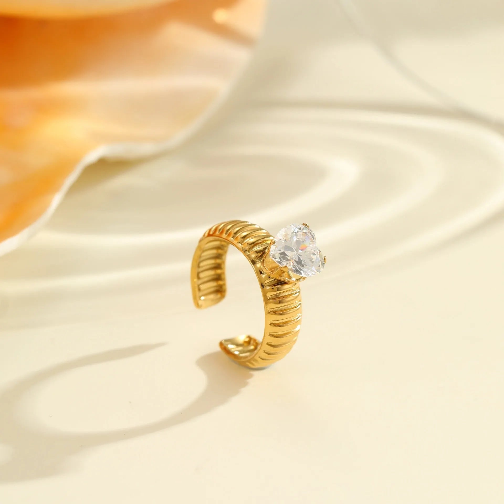 Gold inlaid zircon geometric heart and drop shape stainless steel ring on white background.
