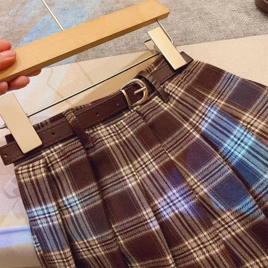 A girls' plaid pleated skirt in an A-line style, shown in a casual setting.