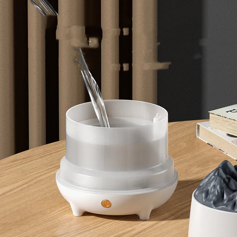 Black volcano-shaped ultrasonic humidifier with USB cable on a wooden table, emitting a plume of mist.