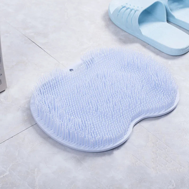 Orange suction cup bath brush with silicone bristles for foot and back cleaning on a bathroom floor.
