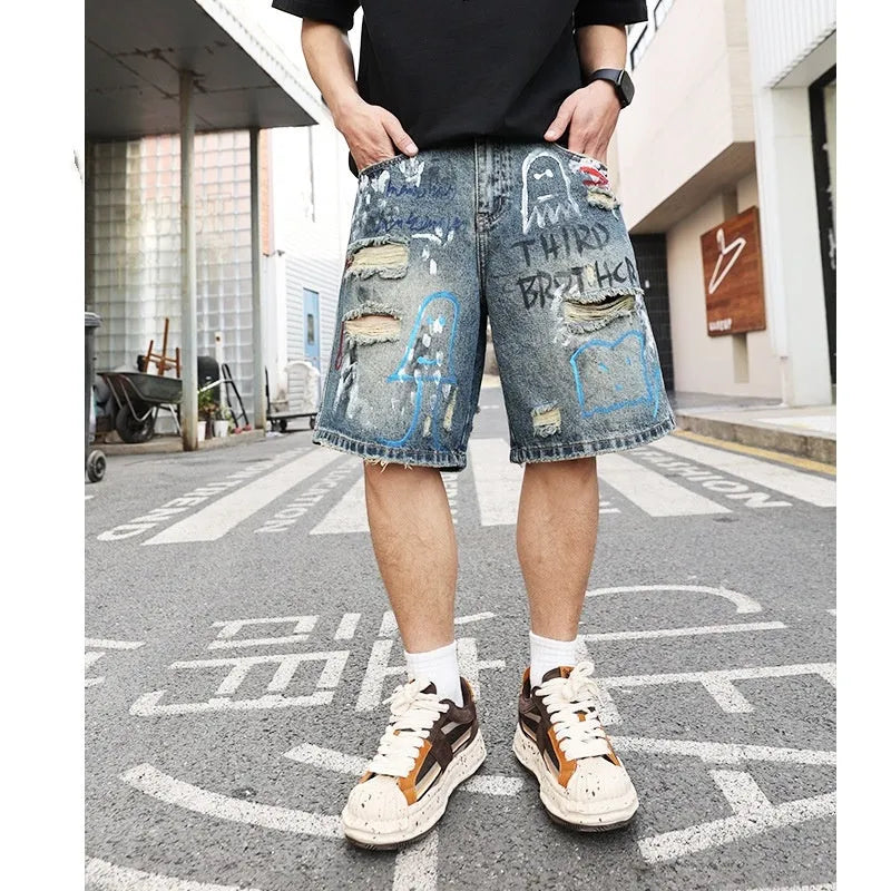 Blue men's ripped denim shorts with a graffiti pattern and zipper fly, laid flat.