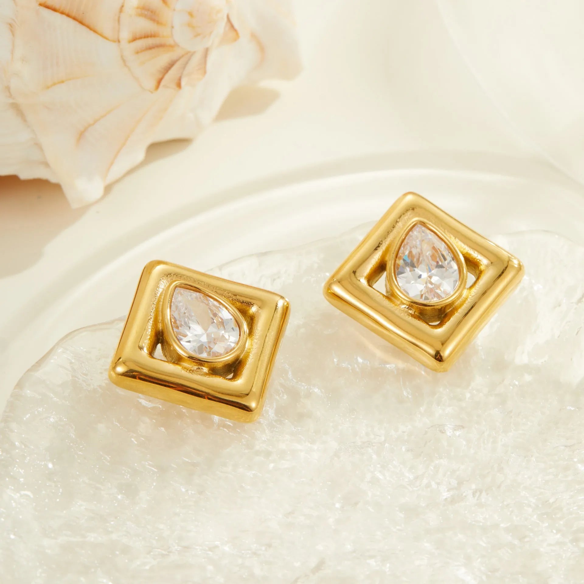Gold geometric stud earrings with inlaid water drop zircon on white background.