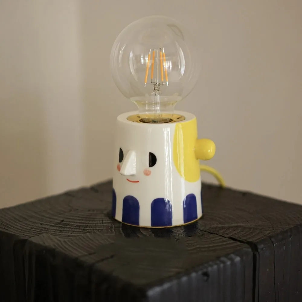 Handmade ceramic bedside lamp with a ball headlight design on a table.