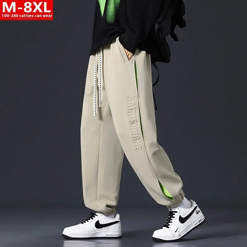 Man wearing loose grey-green cotton trousers with banded ankles and stitching detail.