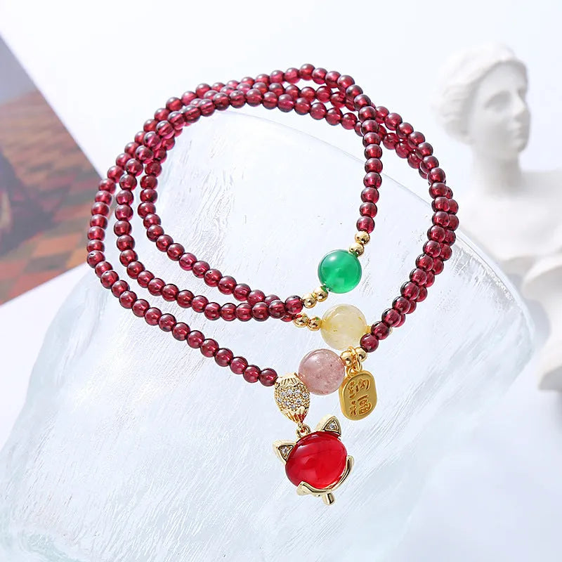 Purplish red garnet fox charm bracelet with adjustable rope on a wrist.