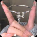 Silver adjustable bracelet with a fixed bow charm on a wrist.