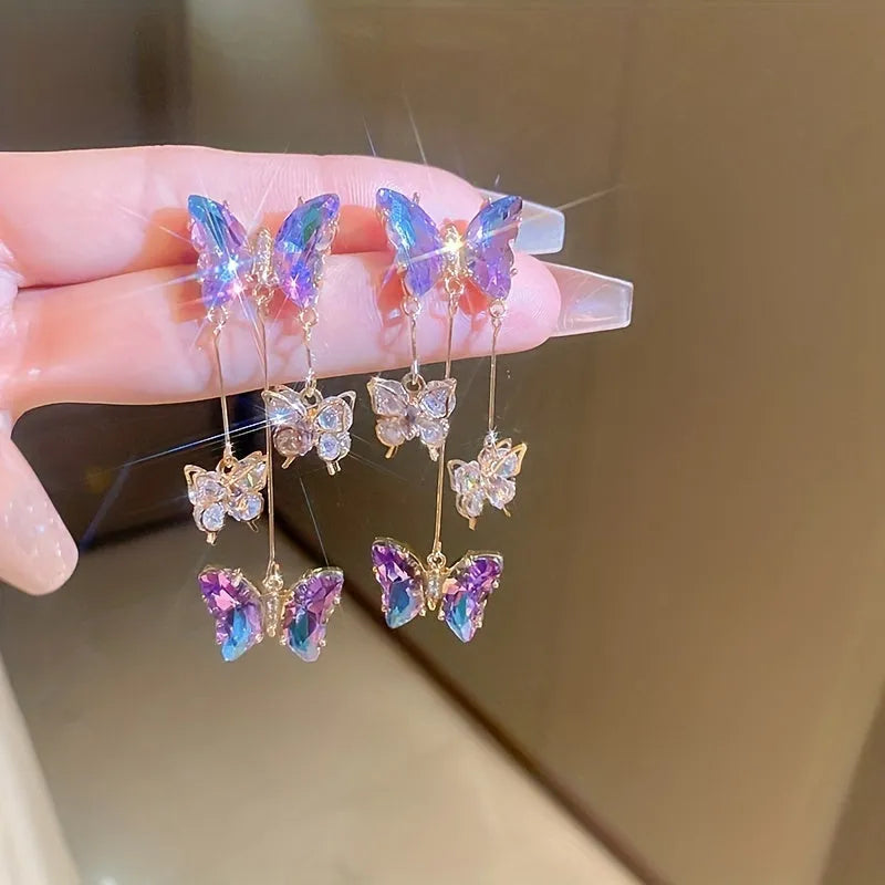 Silver needle style drop earrings with blue purple butterfly, crystals, and a tassel.