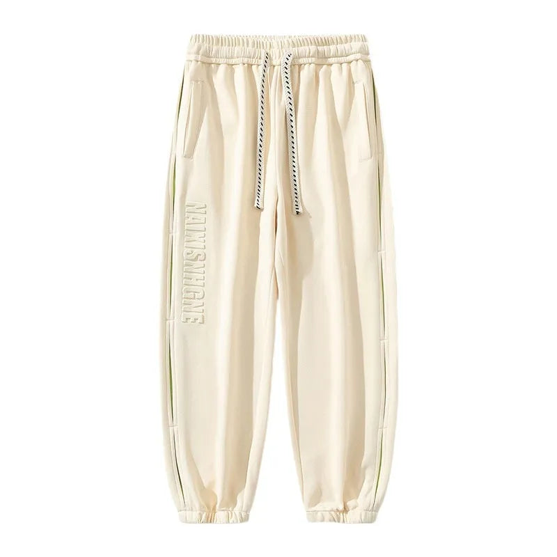 Man wearing loose grey-green cotton trousers with banded ankles and stitching detail.