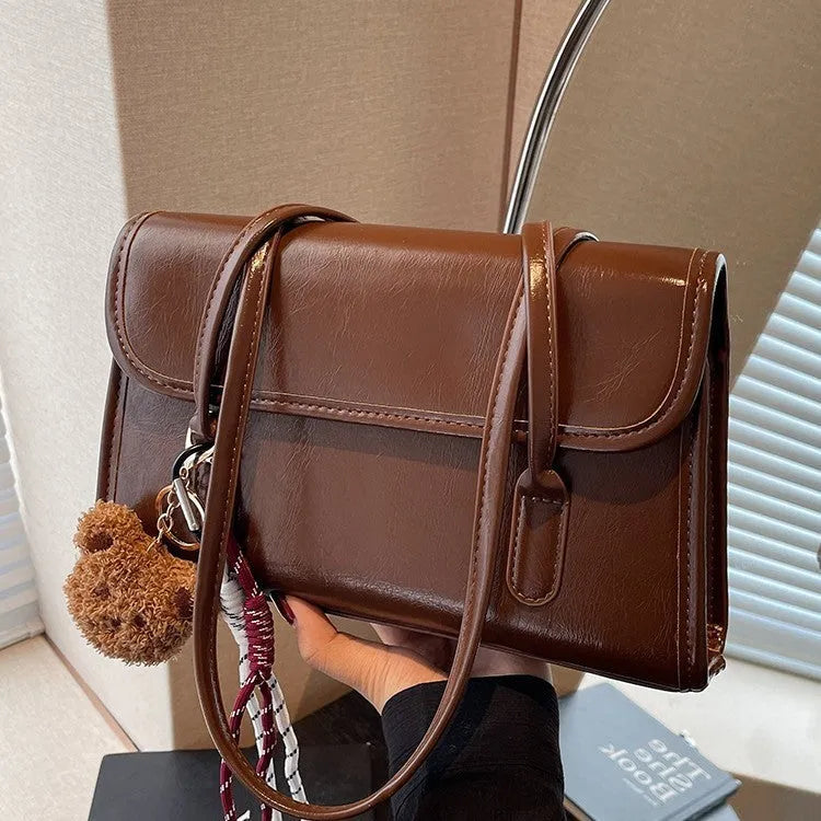 Brown women's square PU shoulder bag with a detachable pendant on a table