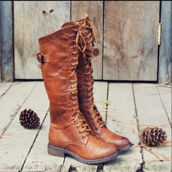 Women's black cross strap knight boots made from PU leather, showing the knee-high design and strap detail.