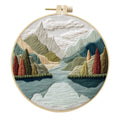 DIY embroidery kit with landscape-printed cotton fabric, embroidery hoop, needles, and coloured thread spools.
