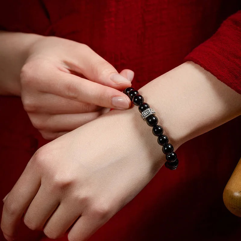 Dark 8mm obsidian bracelet with carved Chinese zodiac animal design on a wrist.