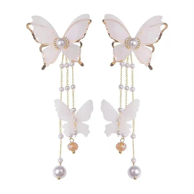 Close-up of white butterfly-shaped earrings with dangling lace tassels, pearl beads, and clear rhinestone accents.