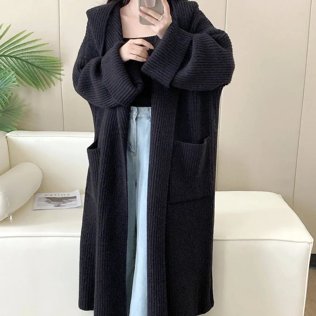 A long, loose grey hooded cardigan coat for women on a hanger, showing its length and raglan sleeves.