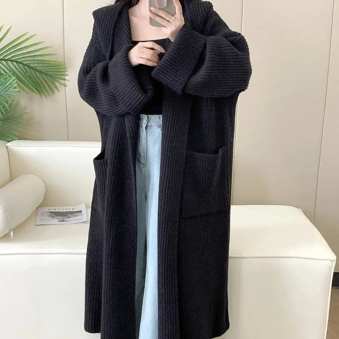 A long, loose grey hooded cardigan coat for women on a hanger, showing its length and raglan sleeves.